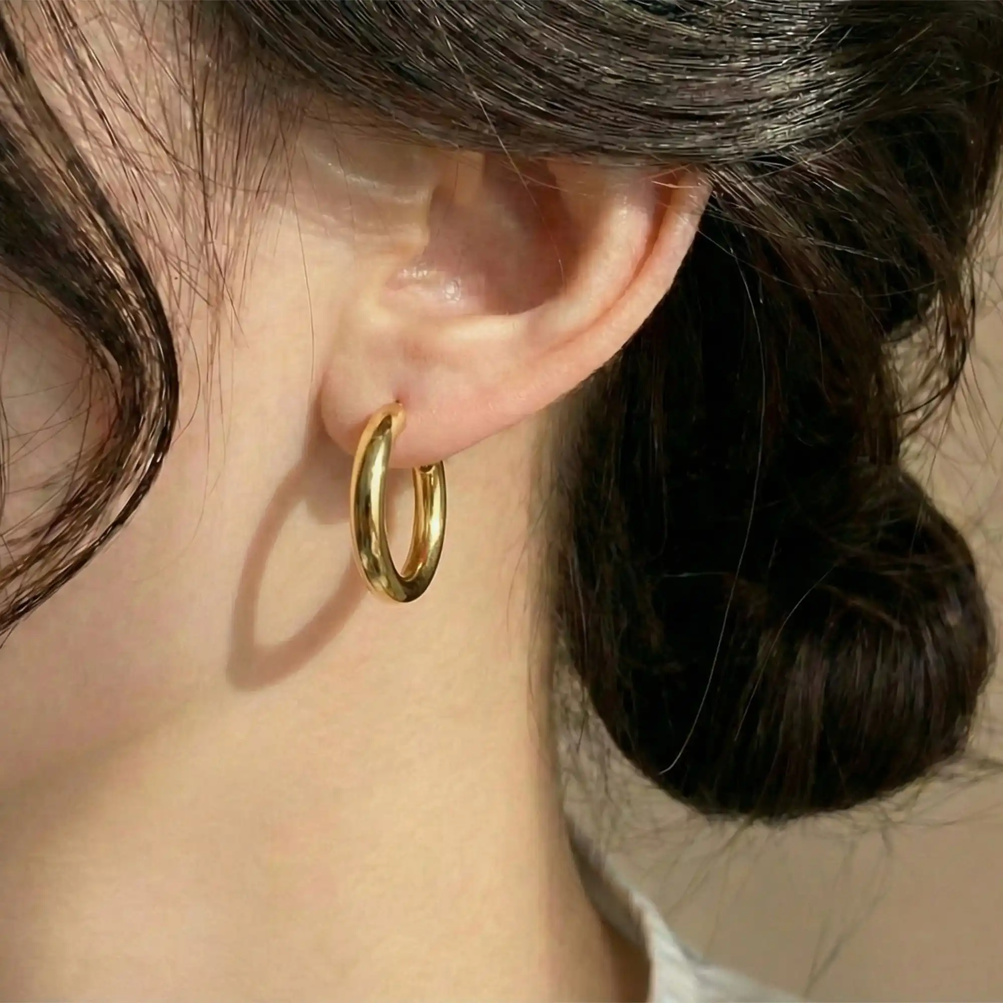 Close-up of a woman wearing a smooth, polished gold huggie hoop earring without a charm.